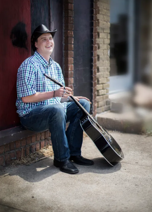 Blind Joe, sitting in a doorway holding his guitar.