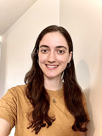 Female with long brown hair wearing an orange top smiling at the camera