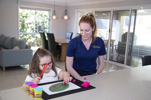 A young girl plays with tactile blocks sitting next to a woman