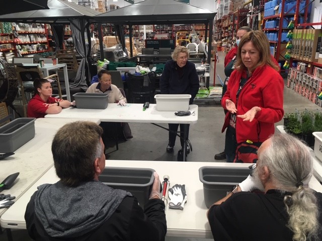 A woman stands in front of two seated people an provides gardening tips