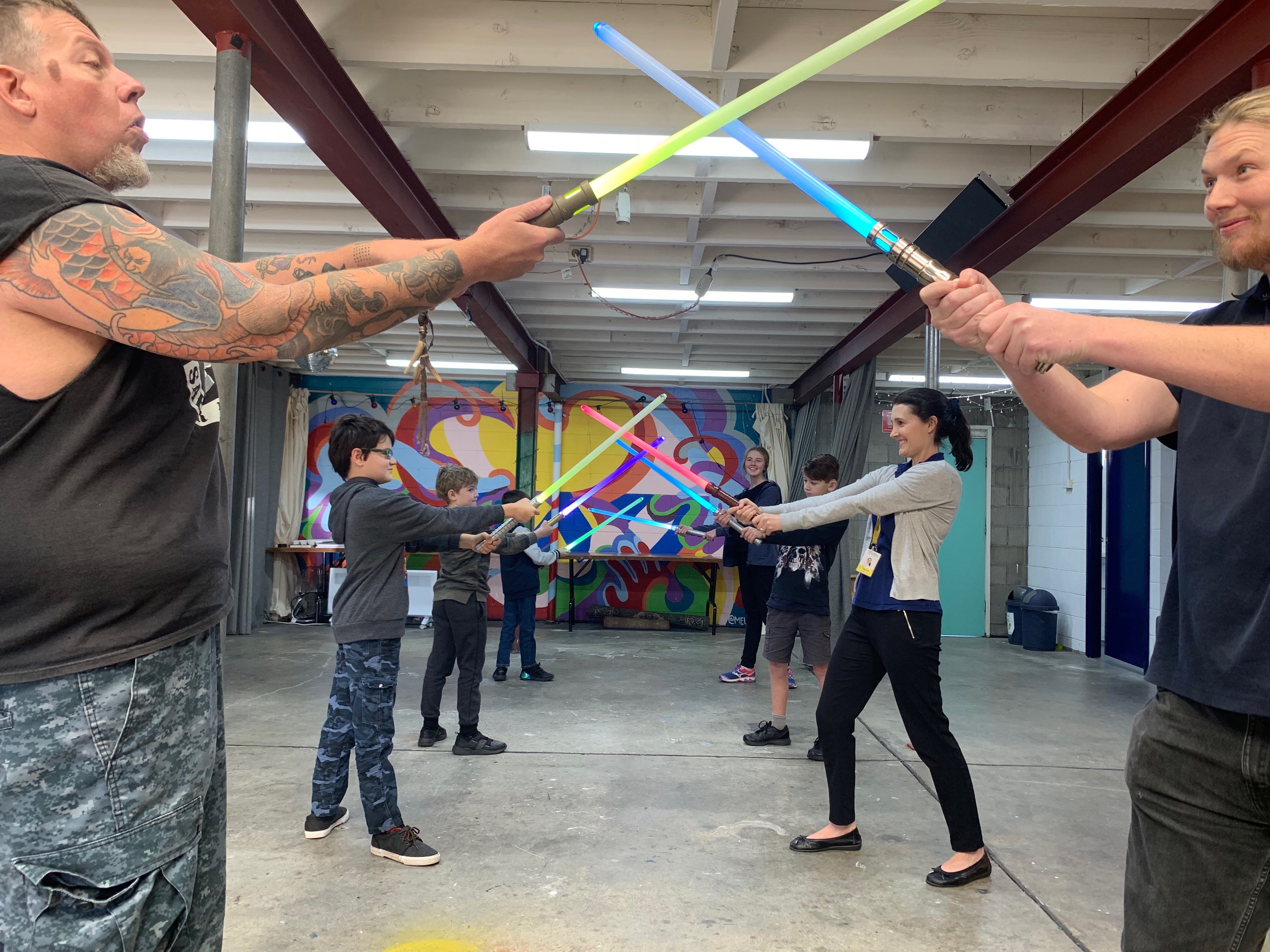 Kids and teachers standing across from each other, light sabers crossing over with each other