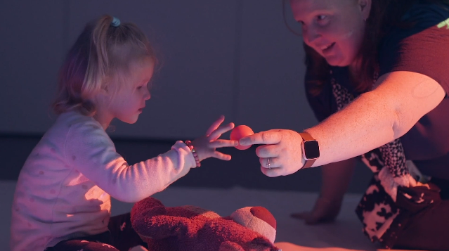 Child reaches for ping pong ball, handed to her by a Vision Australia worker. 