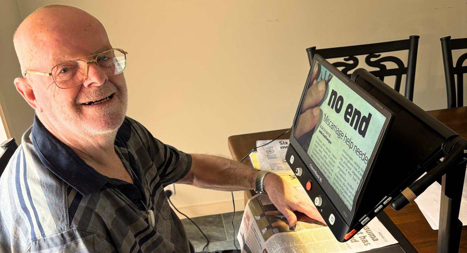Bob is using a magnification device to read a newspaper.