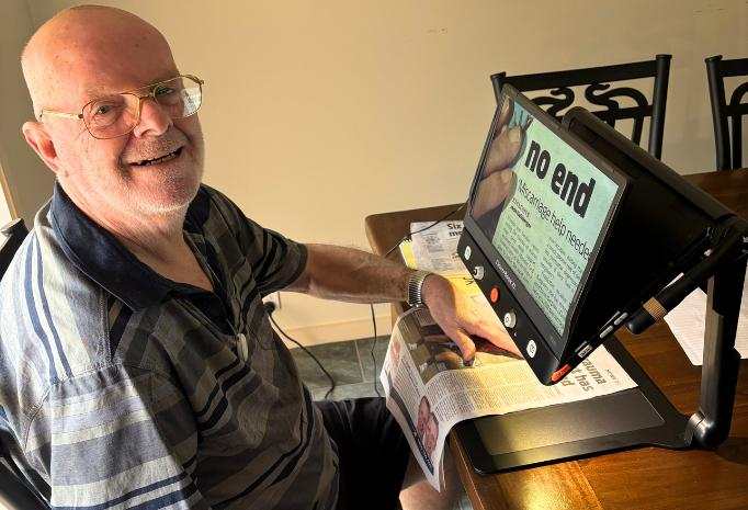 Bob is using a magnification device to read a newspaper.