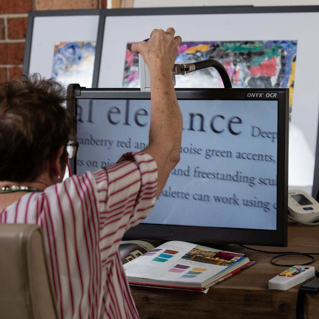 A Vision Australia client uses a digital magnifier as she reads a book.