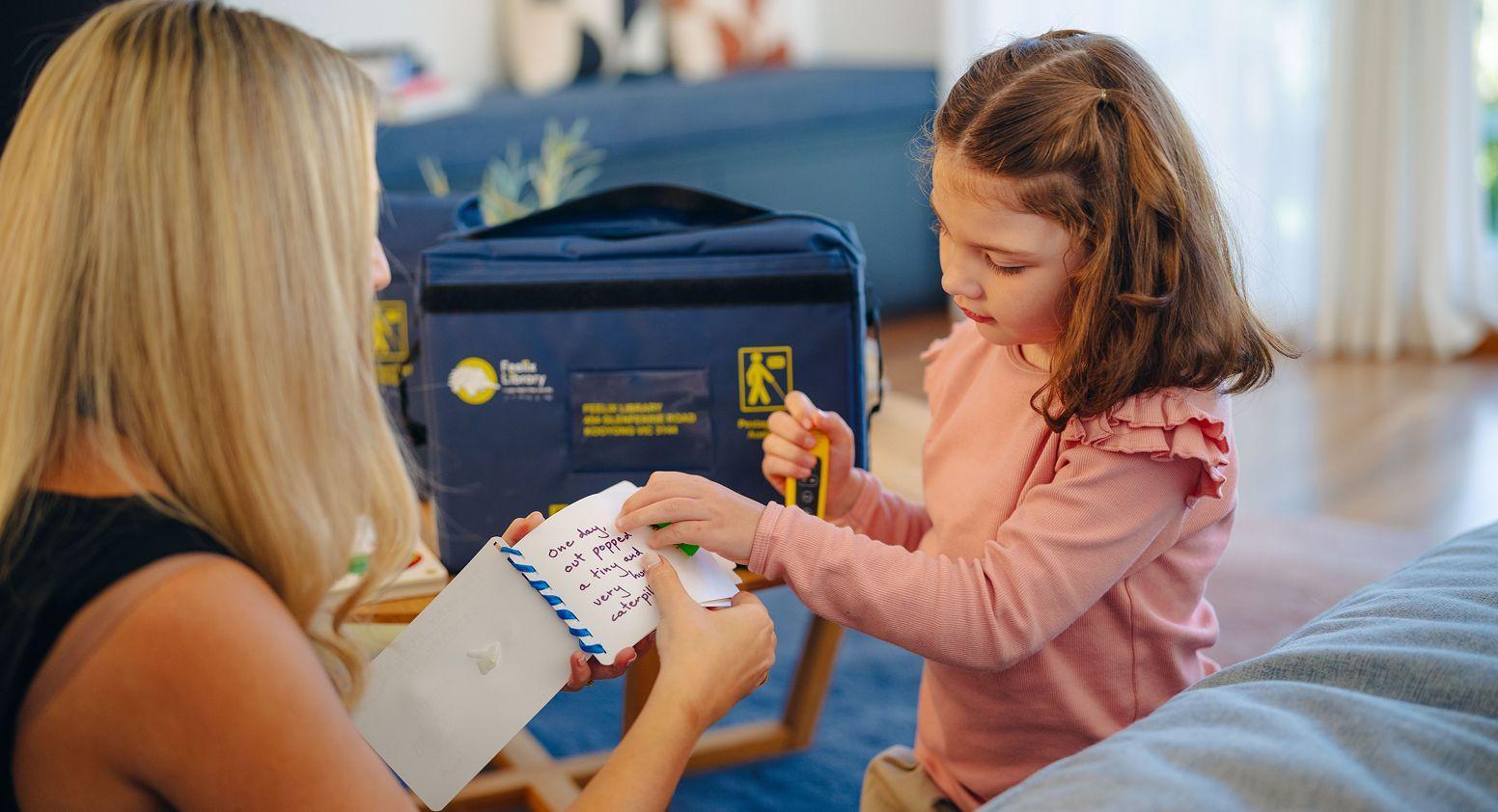 A child is feeling a book, which is being held by an adult