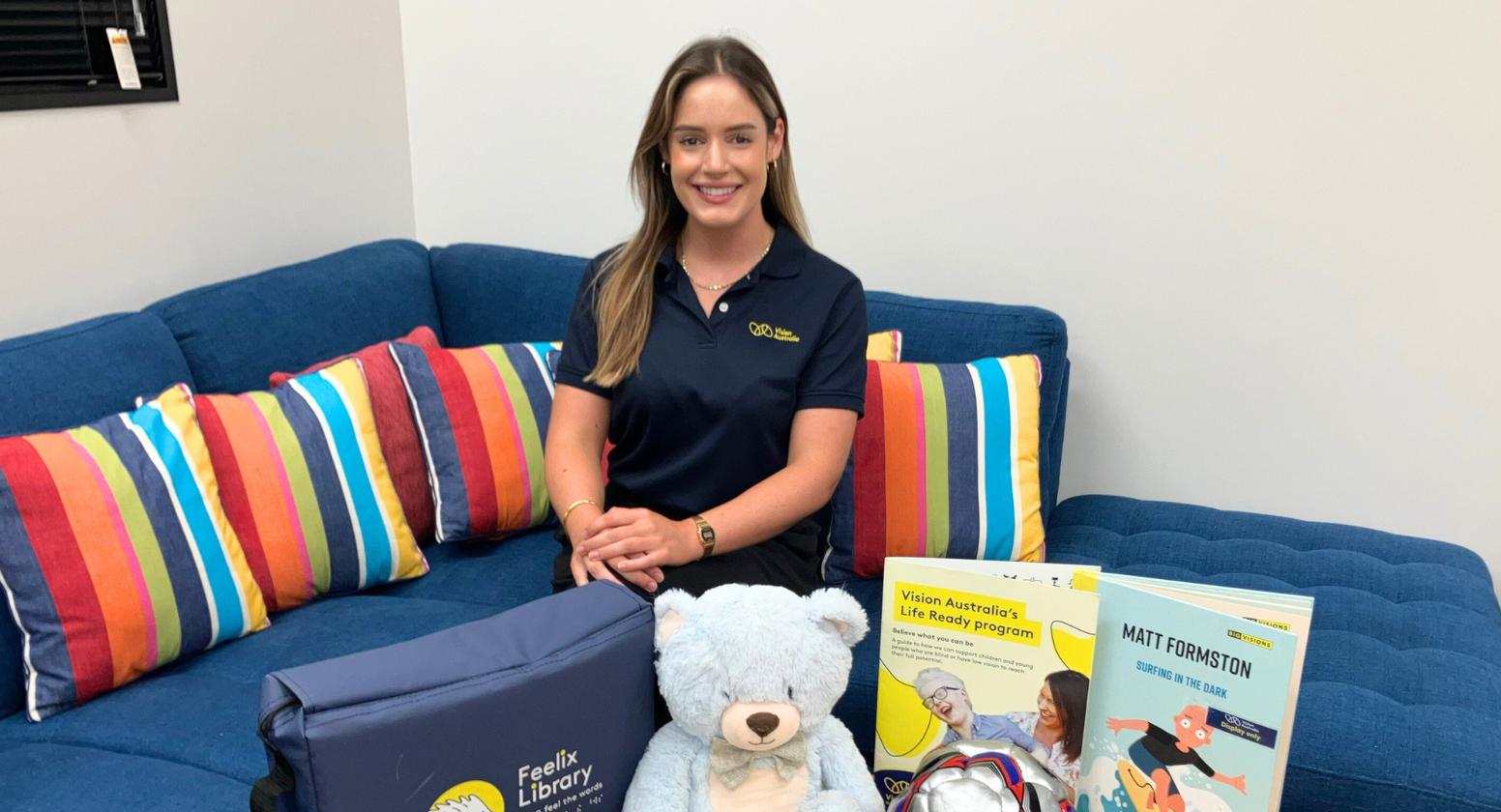 Kaylie, Paediatric occupational therapist Kaylie is sitting on a blue couch, surrounded by toys and games she uses in her practice