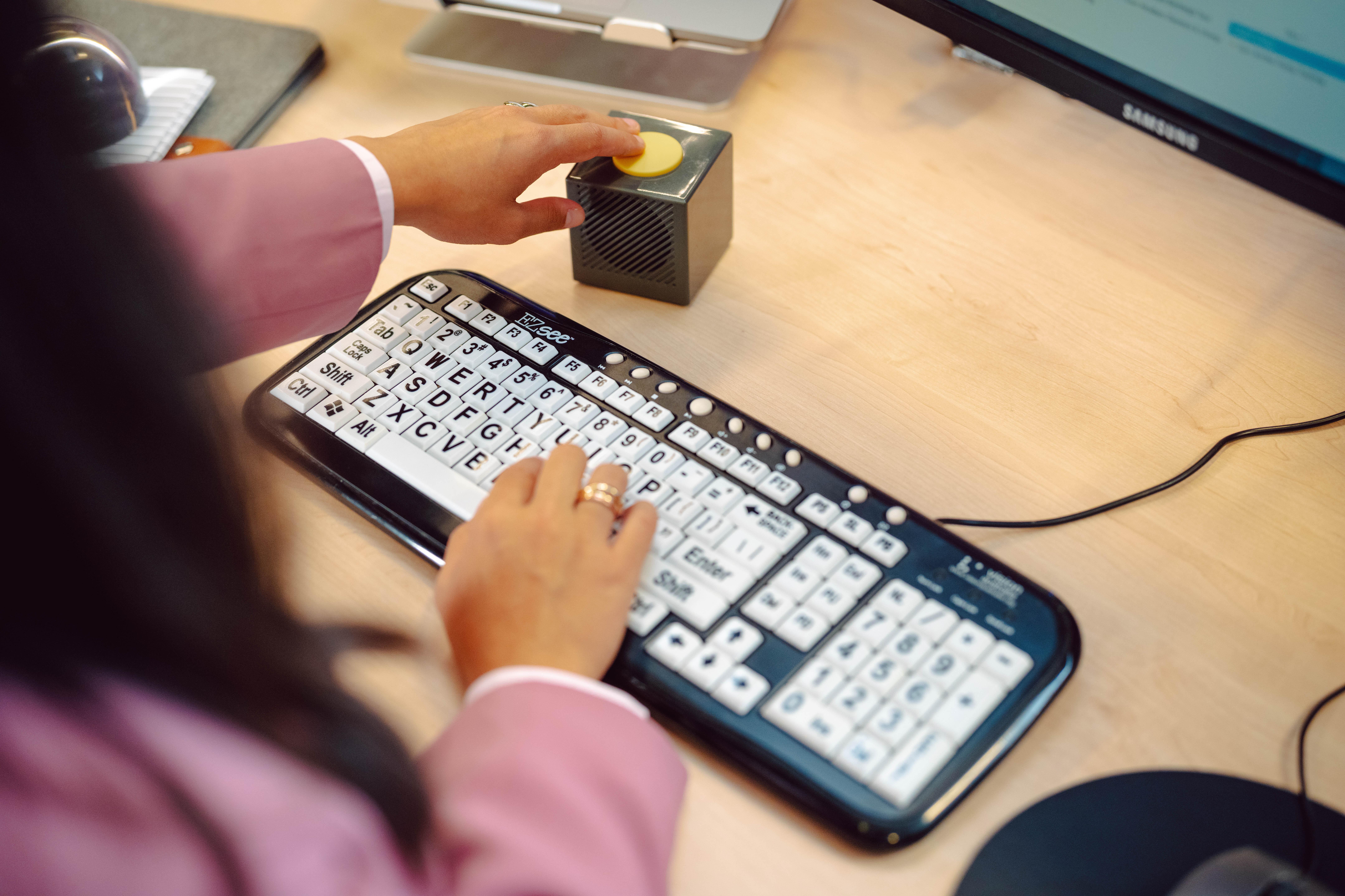 A woman types on a high contrast keyboard, with white buttons and large print black text.