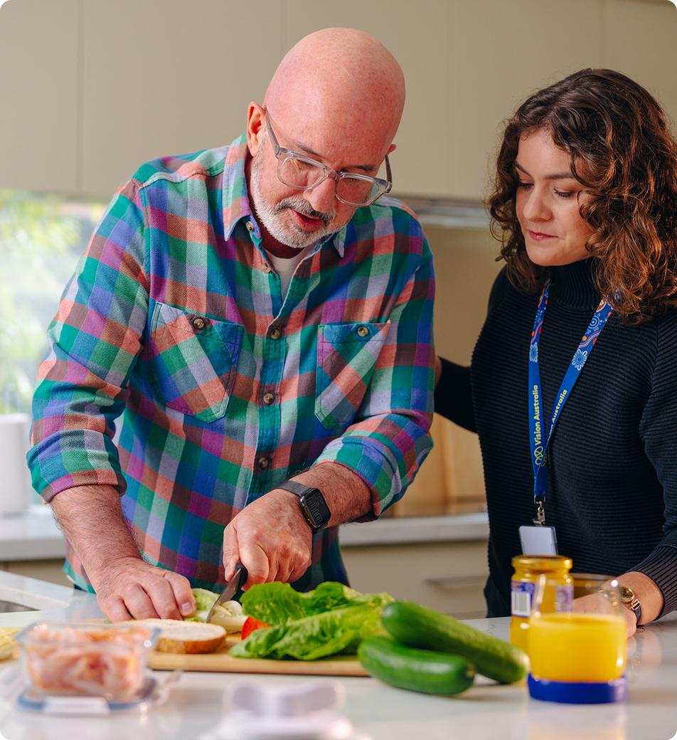 Vision Australia client Stephen Mooney prepares a sandwich in the kitchen with support from Vision Australia OT Andrea Cherny.